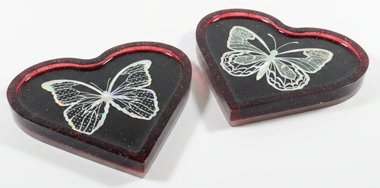 Two heart-shaped resin trays with a dark red translucent border and a holographic butterfly design in the center, displayed on a white surface.
